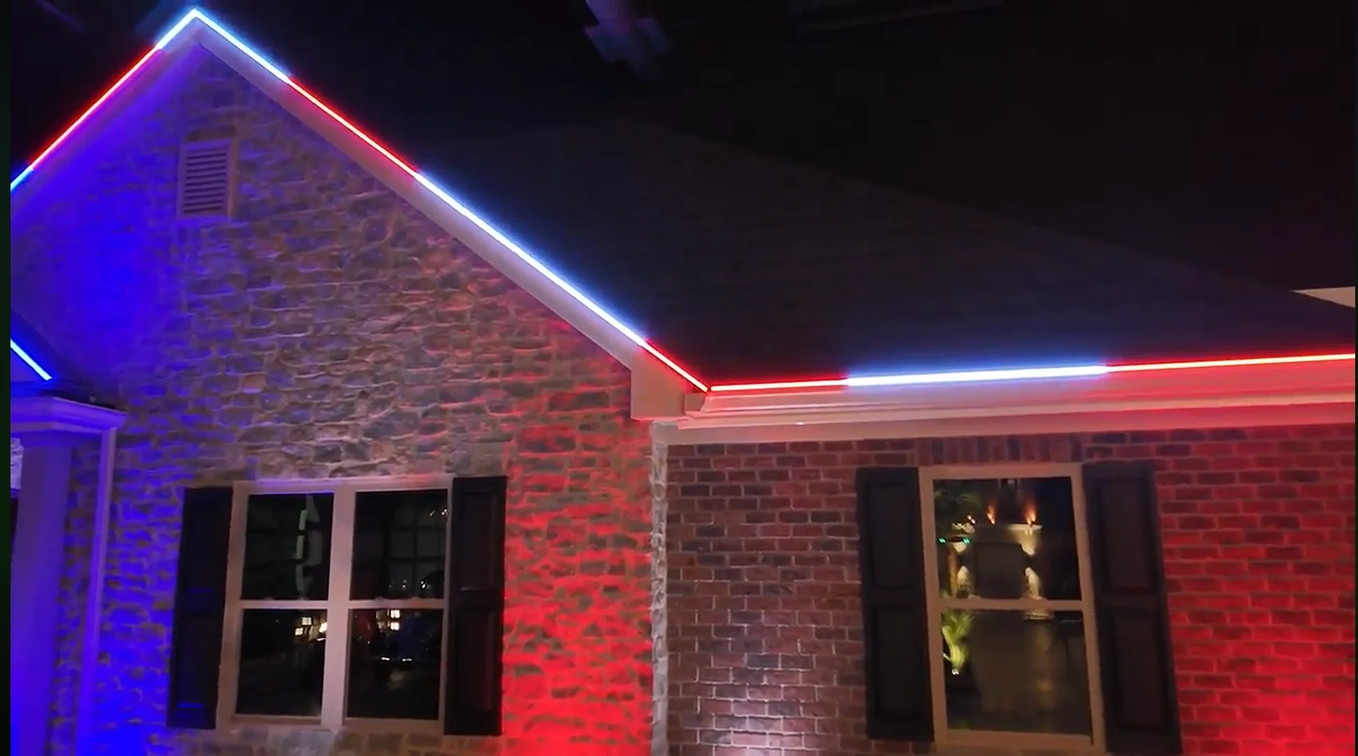 Roofline lighting glowing red, white, and blue across a stone and brick home at night