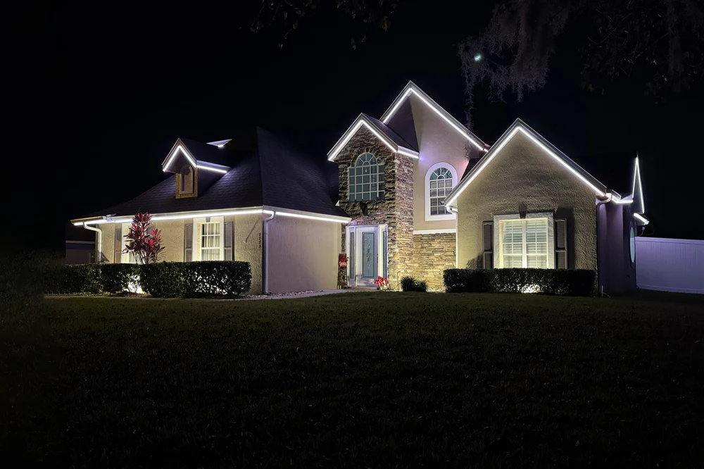 Warm white permanent lighting along the rooflines of a stucco home at night
