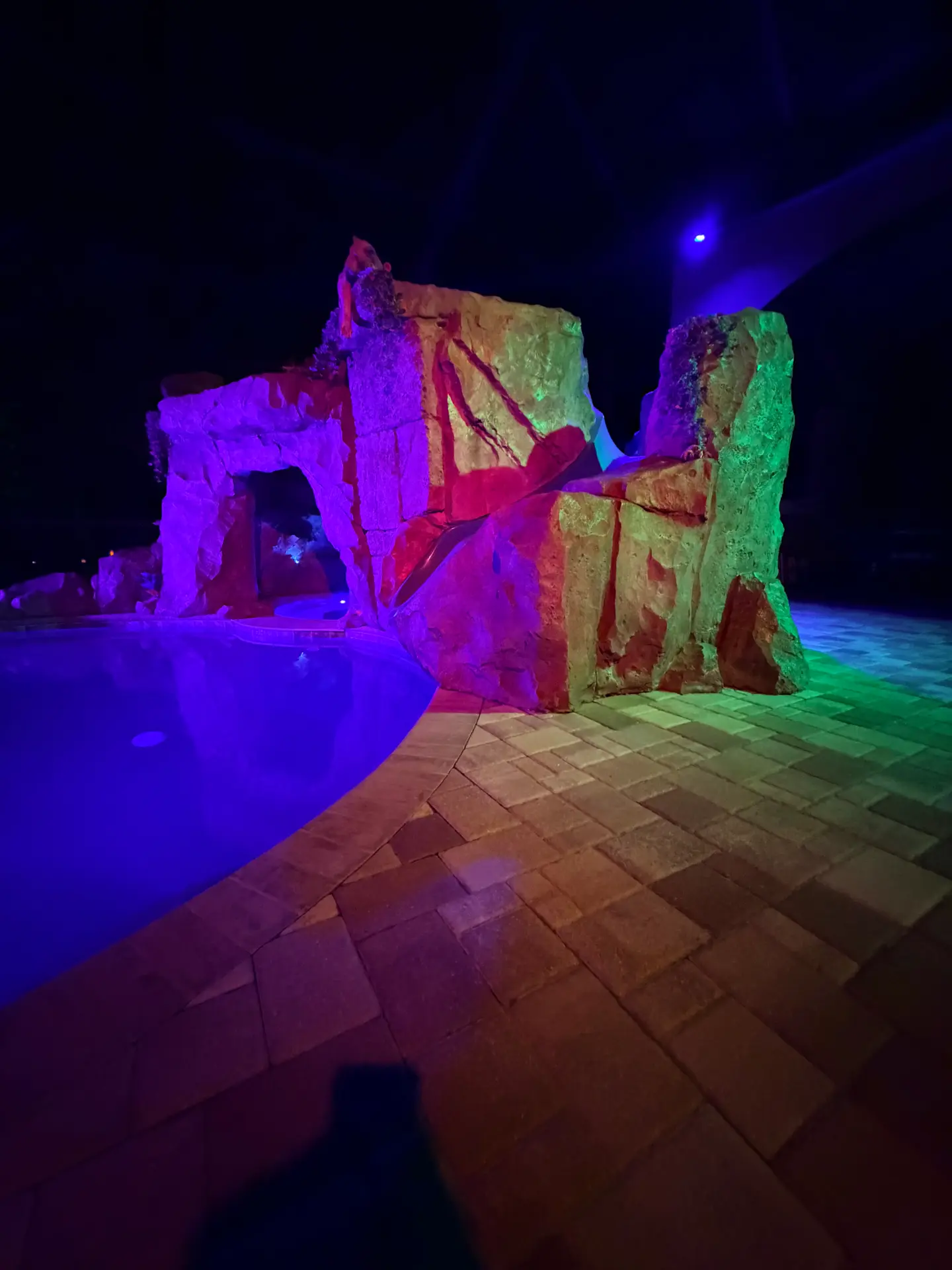 Pool grotto and waterfall feature washed in colored lighting at night