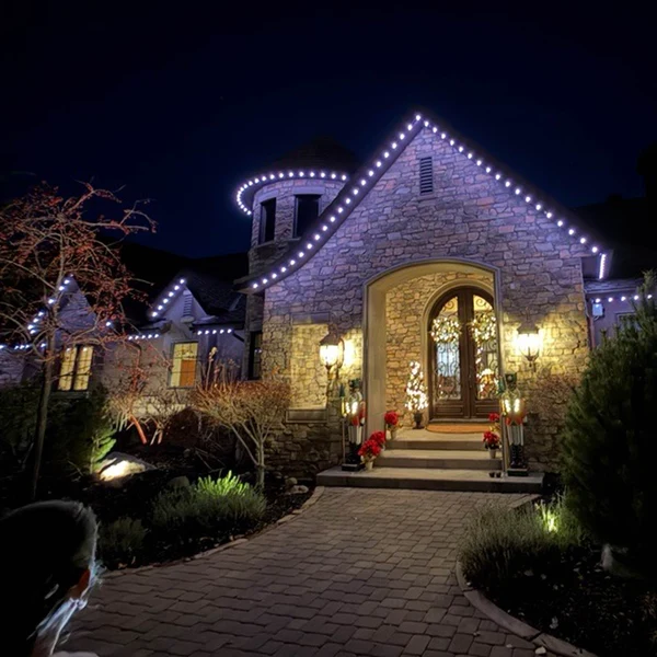 Permanent lighting tracing the gables and entry walk of a stone home at night